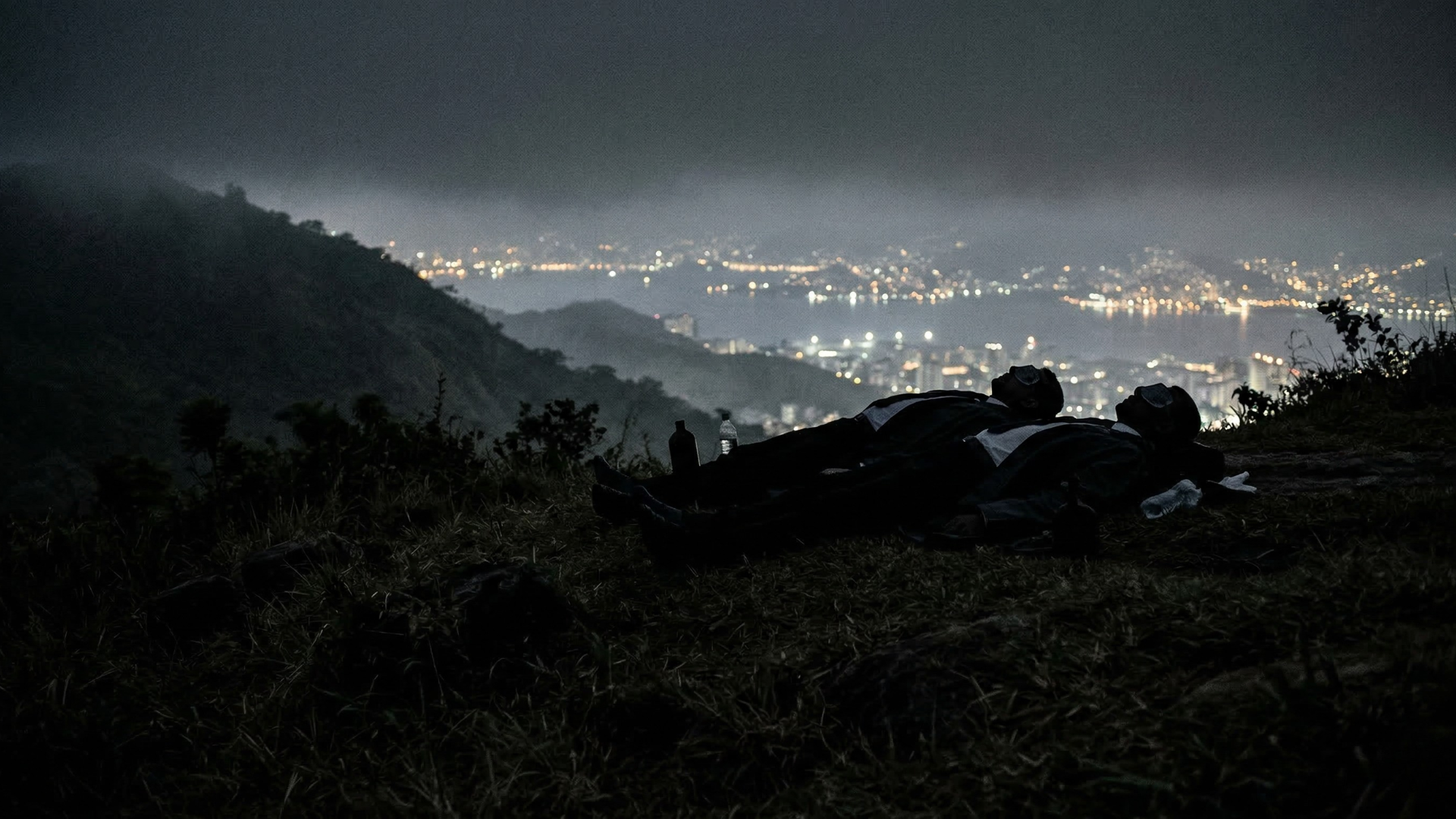 Dos cuerpos en la cima de una colina con las luces de Niteroi de fondo